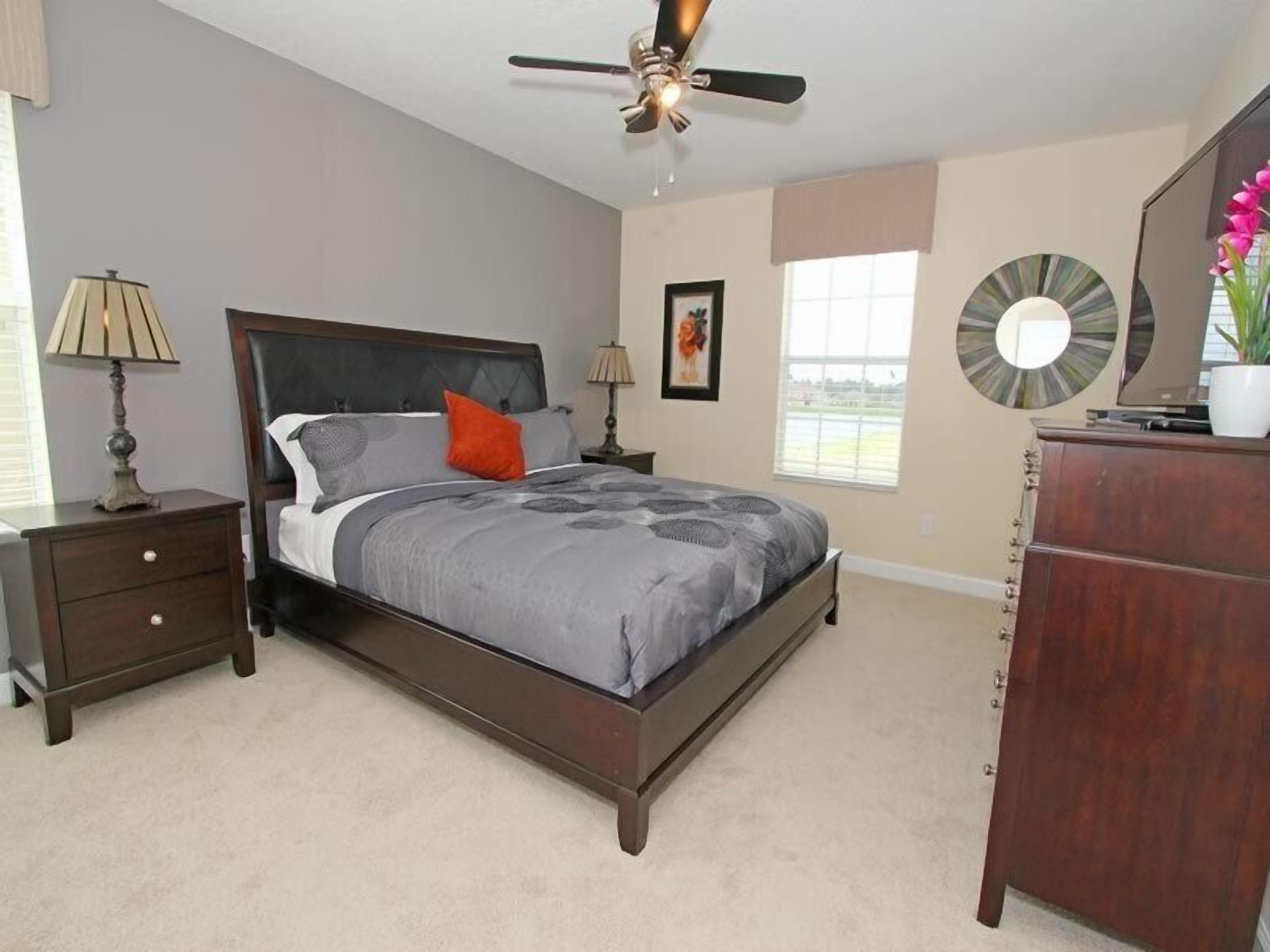 A bedroom with a bed, nightstands, a dresser, a ceiling fan, and a window.