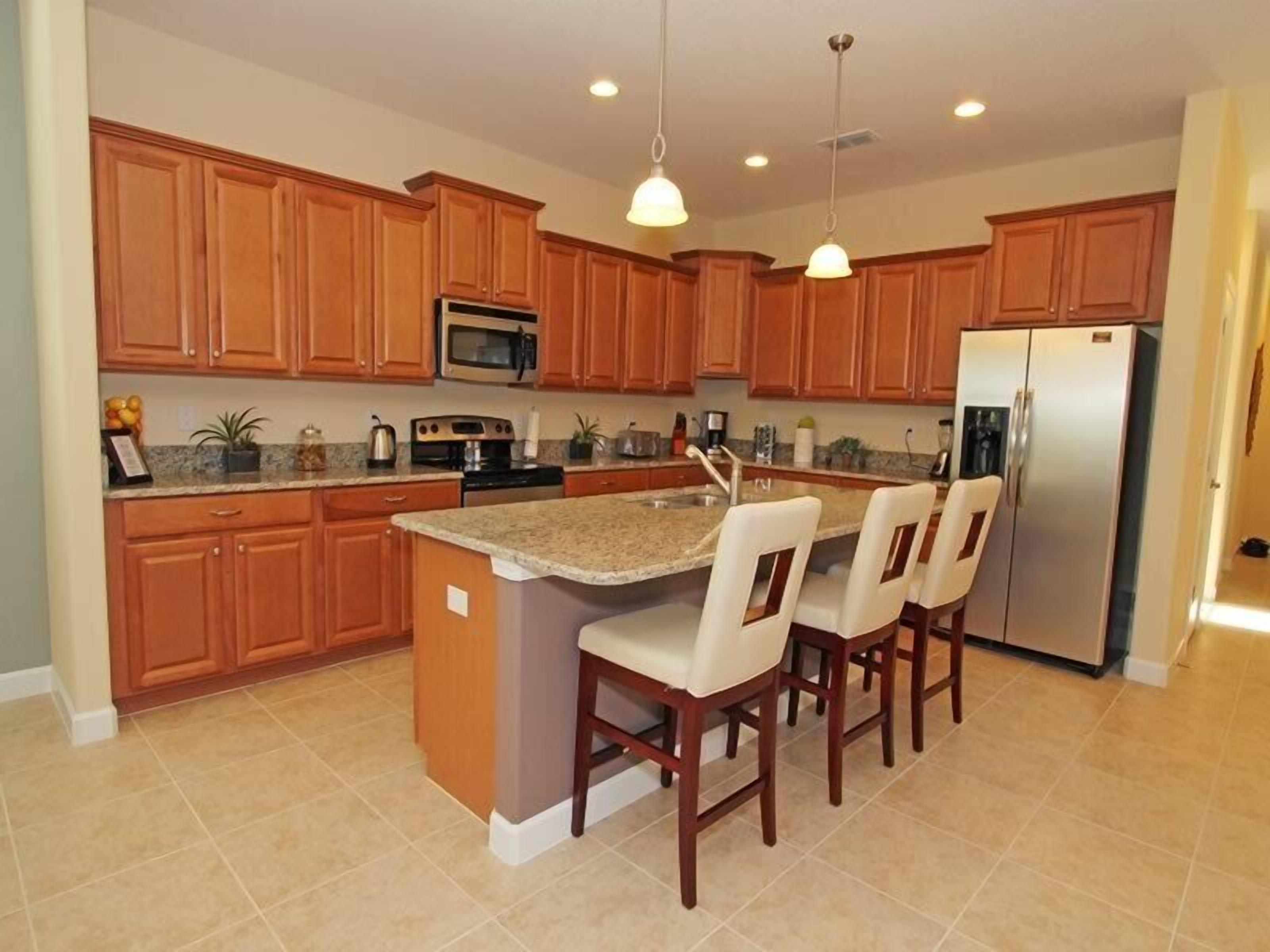 A kitchen with wooden cabinets, a stainless steel refrigerator, a microwave, and a granite countertop.
