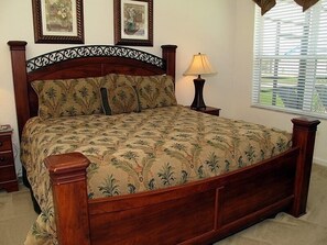 A bedroom with a wooden bed, floral bedspread, two framed pictures on the wall, a bedside lamp, and a window with blinds. - Ov2605 - Windsor Hills Resort - 5 Bed 5 Baths Villa (Kissimmee)