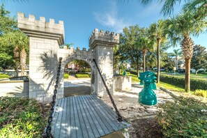 Approach the grand entrance of this majestic castle, flanked by a serene lawn and palm trees.