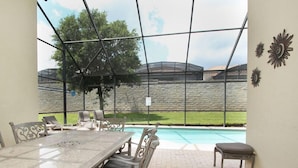 An outdoor patio with a table and chairs, a pool, and a stone wall in the background.
