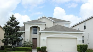 A single-story house with a garage, a front door, and a small front yard with a tree and bushes.