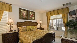A bedroom with a large bed, two bedside tables with lamps, a television on a stand, and a window with curtains.