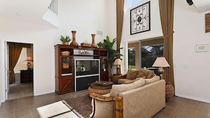 A spacious living room with a large window, a wooden cabinet with decorative items, a beige sofa, and a floor lamp.