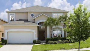 A two-story house with a garage, a small front yard with a palm tree, and a clear sky.