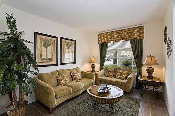 A living room with a sofa set, two lamps, a coffee table, and a large potted plant.