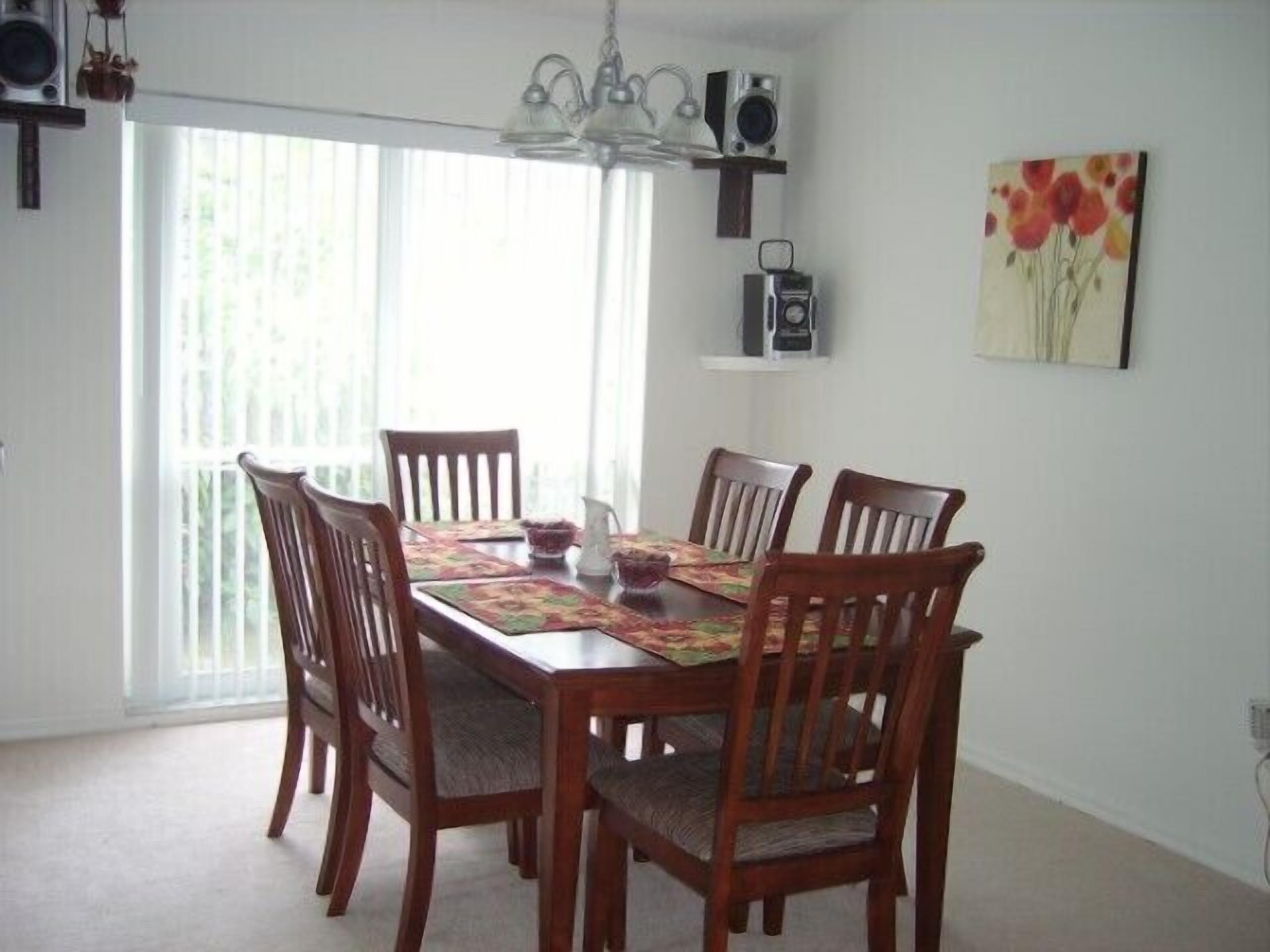 A dining area with a wooden table and chairs, a chandelier, a window with blinds, and a wall-mounted radio.