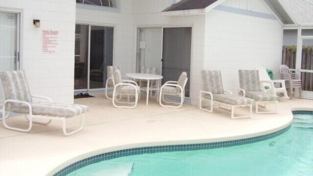 A pool area with lounge chairs and a table, a covered patio, and a sign indicating pool hours. - Ov1761 - Davenport Lakes - 4 Bed 2 Baths Villa (Davenport)