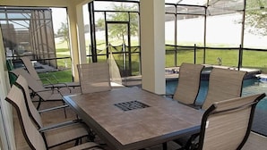 An outdoor patio with a rectangular table and multiple chairs, surrounded by glass walls and a view of a swimming pool. - Ov2545 - Windsor Hills Resort - 5 Bed 5 Baths Villa (Kissimmee)