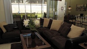 A living room with a dark brown sectional sofa, a glass coffee table, and a vase with white flowers. - Ov2545 - Windsor Hills Resort - 5 Bed 5 Baths Villa (Kissimmee)