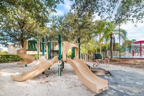Explore the playground's multi-colored slide and climbing elements amidst lush trees and a secure fenced area.