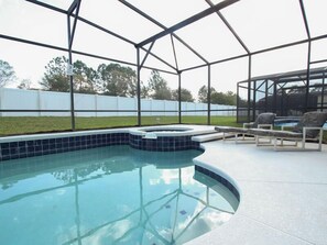 Une piscine avec un jacuzzi, entourée d’un patio couvert agrémenté de chaises longues.
