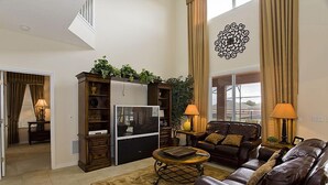 A living room with a brown leather sofa, a coffee table, a TV, and a bookshelf. - Ov1969 - Emerald Island - 6 Bed 5 Baths Villa (Kissimmee)