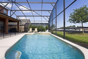 A swimming pool with a glass enclosure, surrounded by a patio area with chairs and a view of the surrounding landscape. - Ov1969 - Emerald Island - 6 Bed 5 Baths Villa (Kissimmee)