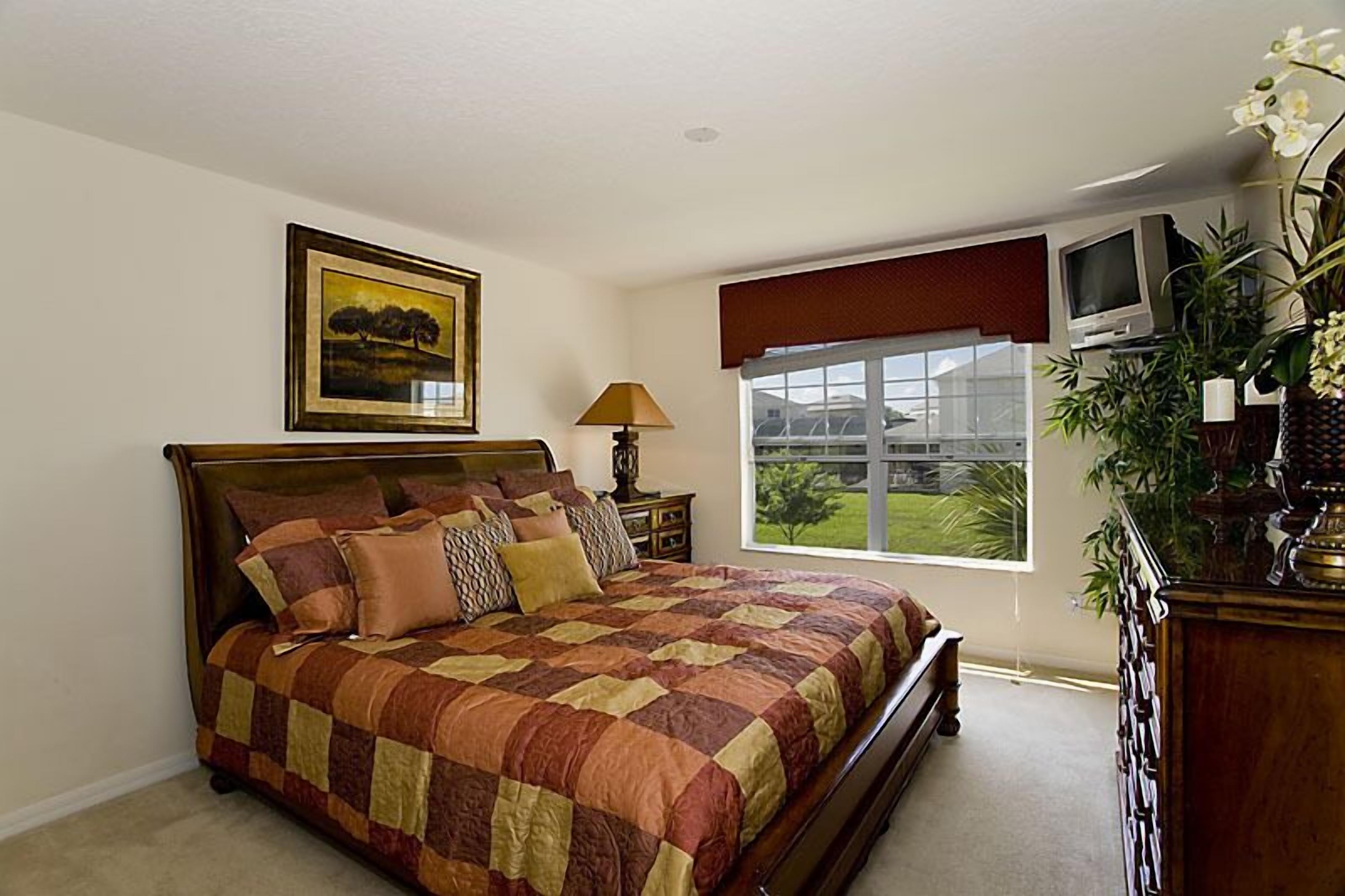 A bedroom with a large bed, a TV, a window with a view of greenery, and a painting on the wall.