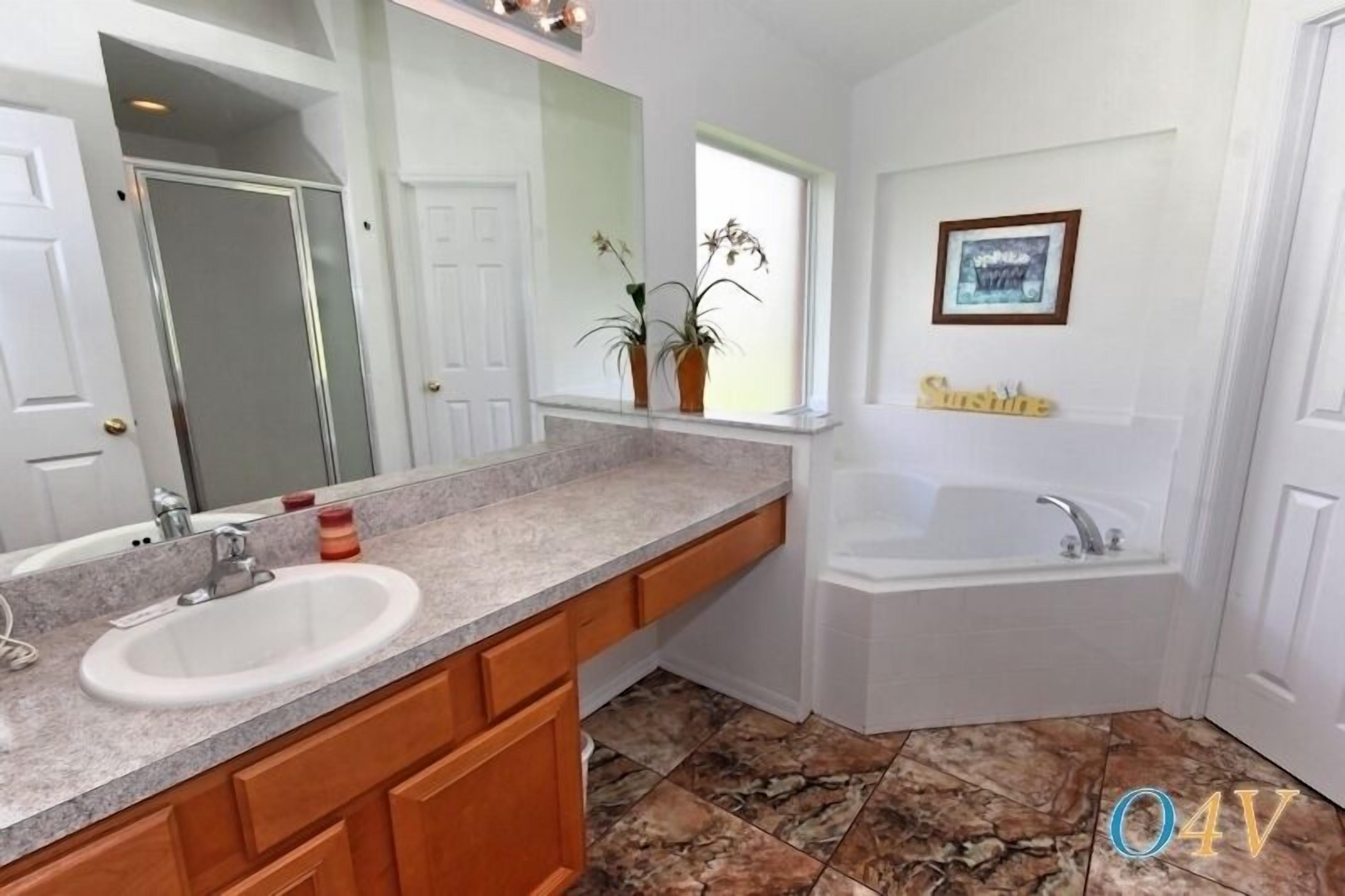 A bathroom with a large mirror, a sink, a bathtub, and a window with plants.