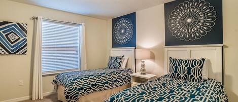 A bedroom with two beds, a window with blinds, a ceiling light, and decorative wall art.