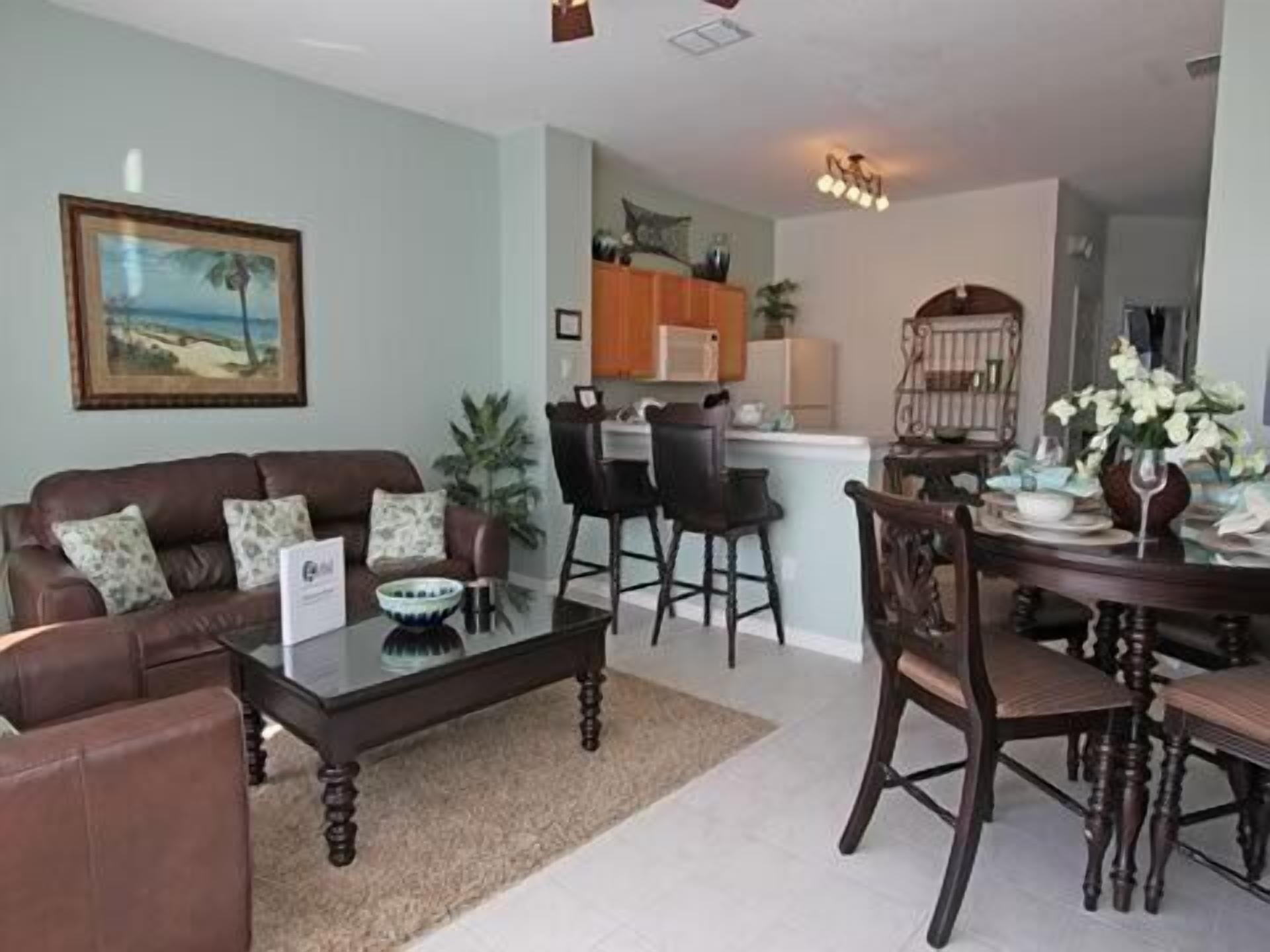 A living room with a brown leather sofa, a glass coffee table, and a dining area with a wooden table and chairs.