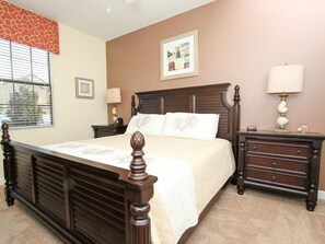 A bedroom with a large bed, a nightstand, a dresser, and a window with blinds. - Ov2858 - Champions Gate Resort - 9 Bed 5 Baths Villa (Davenport)