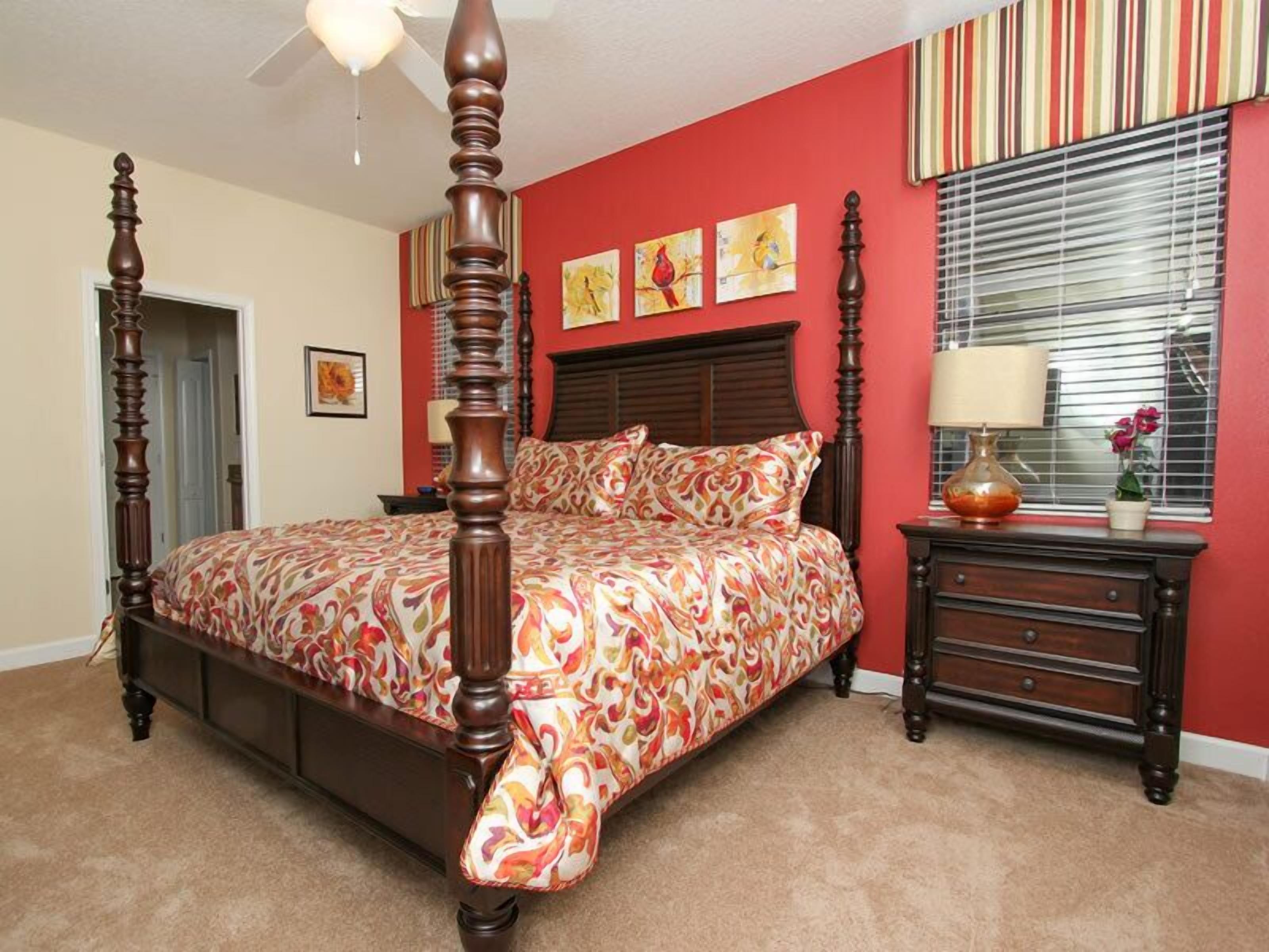 A bedroom with a four-poster bed, a nightstand, a lamp, and artwork on the walls.