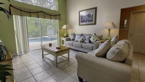 A living room with a sofa, a coffee table, and two lamps. There is a door and a window with curtains.