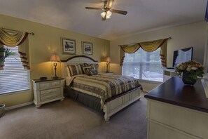 Une chambre à coucher comprenant un lit, des tables de chevet, un ventilateur de plafond et une commode.