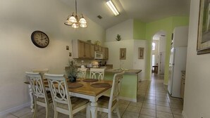 A dining area with a wooden table and white chairs, a kitchen with wooden cabinets, and a green accent wall.