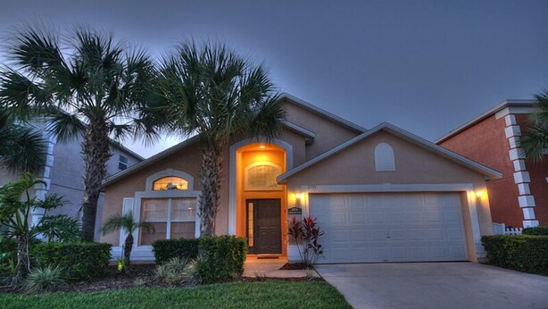 A residential house with a garage, a well-maintained lawn, and palm trees.