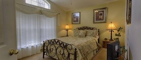 A bedroom with a bed, ceiling fan, two bedside lamps, a TV, and framed pictures on the wall.