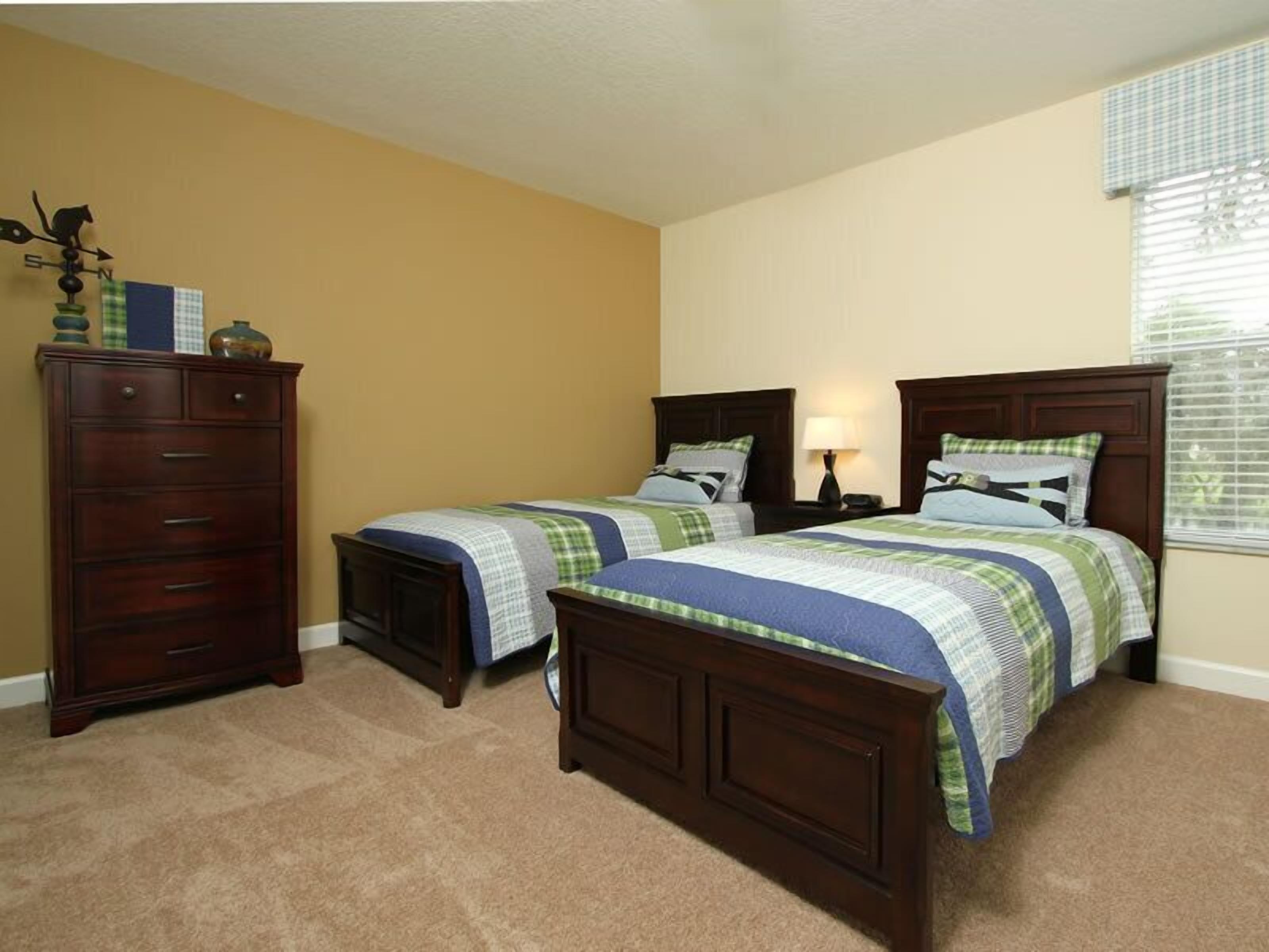 A bedroom with two beds, a dresser, and a window with blinds.
