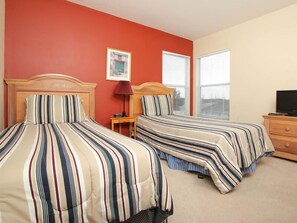 A hotel room with two beds, a wooden dresser, a television, and a window with blinds.
