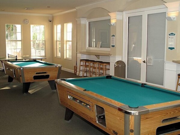A pool table in a room with large windows, a bar area, and a door with a sign.