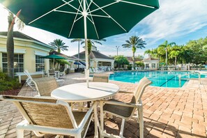 A poolside area with a table and chairs, a large umbrella, and a pool.