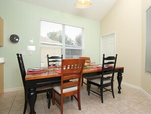 A dining room with a wooden table and chairs, a clock on the wall, and a window with blinds.
