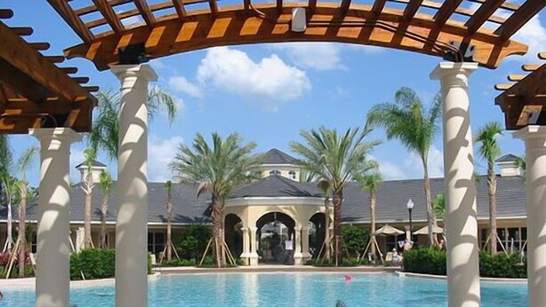 A pool area with two lounge chairs, palm trees, and a building with arches in the background.