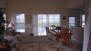 A living room with a sectional sofa, dining table, chairs, and large windows. - Ov2186 - Lindfields - 5 Bed 3 Baths Villa (Kissimmee)