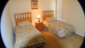 A room with two beds, a nightstand with a lamp, a framed picture on the wall, and a window with blinds. - Ov2186 - Lindfields - 5 Bed 3 Baths Villa (Kissimmee)