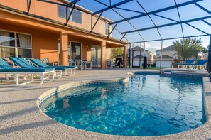 Un área de piscina con sillones reclinables, un porche cubierto y un edificio con ventanas amplias.