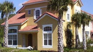 A two-story house with a red-tiled roof, white-framed windows, and a yellow facade. - Ov1484 - Emerald Island - 4 Bed 3.5 Baths Townhome (Kissimmee)