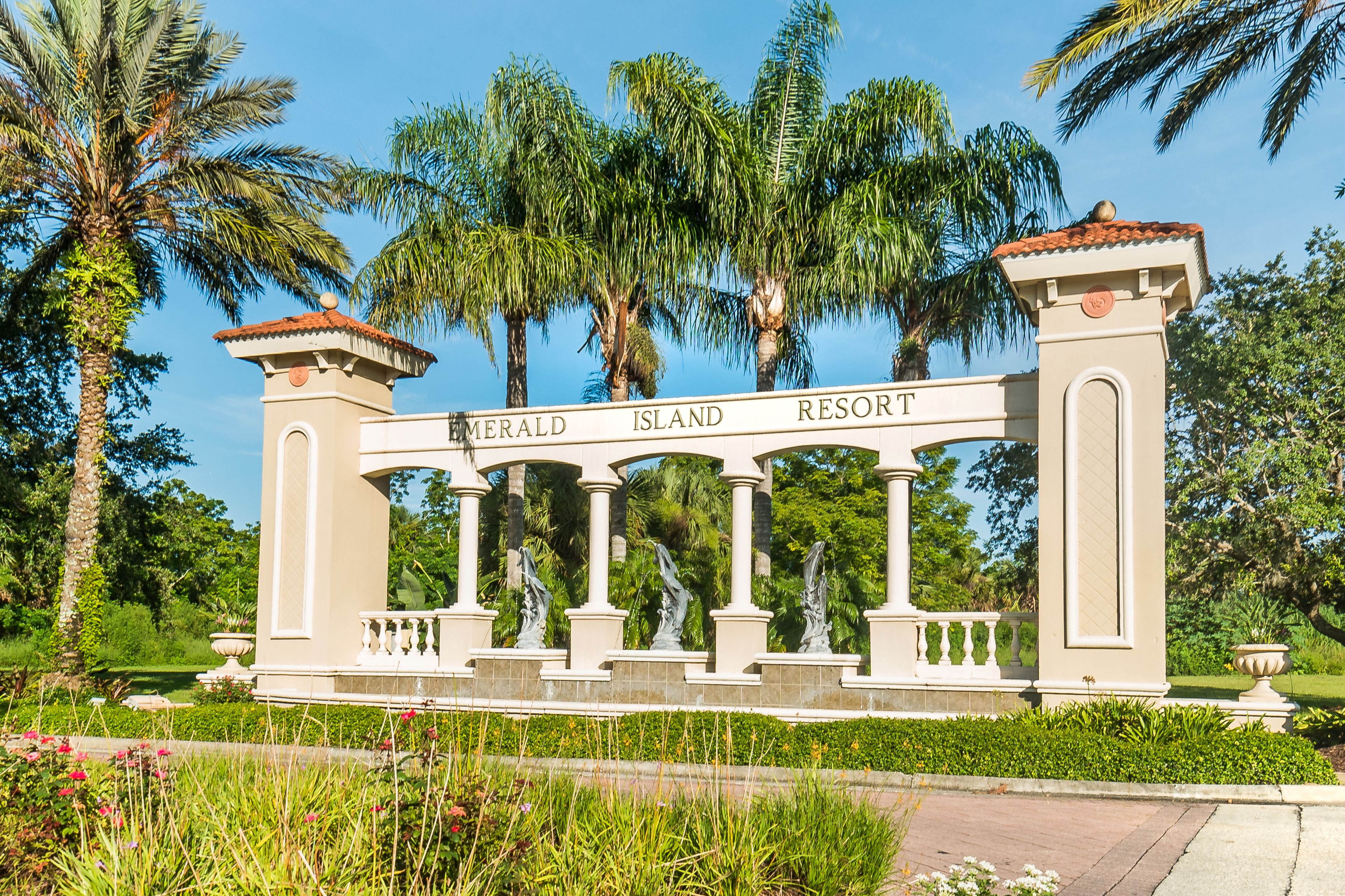 Une enseigne pour le complexe hôtelier Emerald Island, avec une architecture classique, des colonnes et des palmiers en arrière-plan.