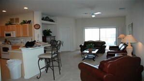 A spacious living room with a brown leather sofa, a dining area with a small table, and a kitchen with wooden cabinets and a microwave. - Ov2749 - High Grove - 4 Bed 3 Baths Villa (Clermont)