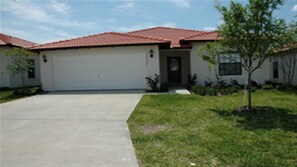 A single-story house with a red-tiled roof, a white garage door, and a small front yard with a young tree.