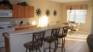 A kitchen with wooden cabinets, a white island with bar stools, a dining area with a table and chairs, and decorative wall art.