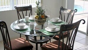 A round glass table with white plates, bowls, and cups, surrounded by dark wooden chairs.