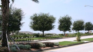 A landscaped area with trees and shrubs, a paved road, and a clear sky.