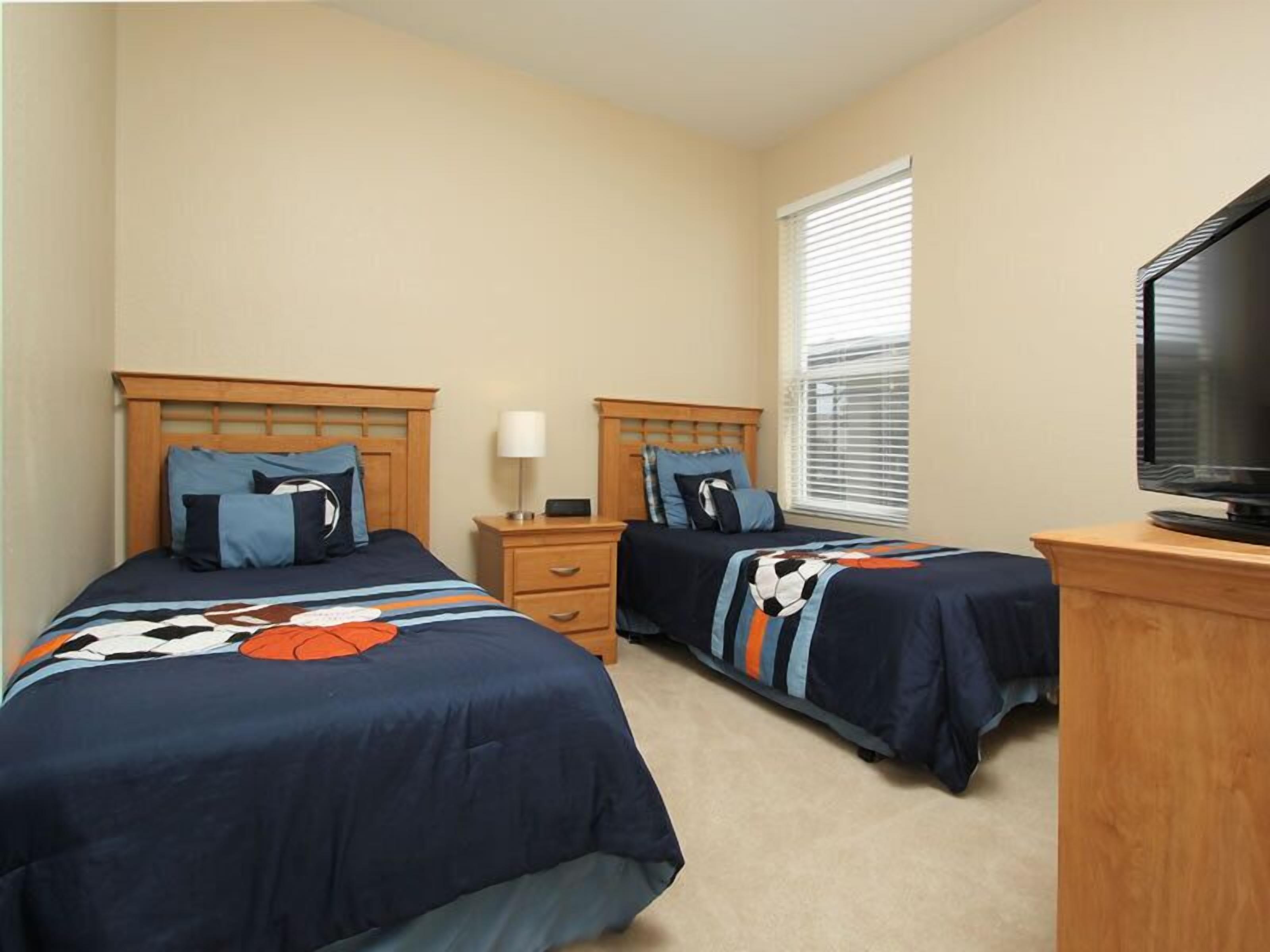 A bedroom with two beds, a TV, and a window with blinds.