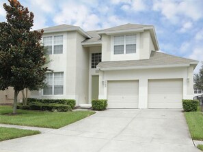 Stunning two-story home with a central entrance, garage doors, and a beautifully manicured lawn.