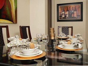 Enjoy meals in this dining area with a glass table, two chairs, and a beautiful framed painting on the wall.