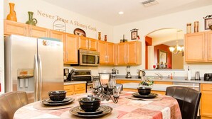 A kitchen with wooden cabinets, a stainless steel refrigerator, a microwave, and a dining table set with black bowls and plates. - Ovm604 - Emerald Island - 6 Bed 5.5 Baths Villa (Kissimmee)