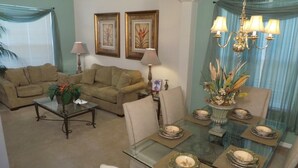 A living room with a sofa, coffee table, and dining table set with plates and a chandelier. - Ov535 - Emerald Island - 7 Bed 4 Baths Villa (Kissimmee)